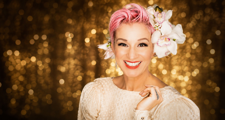 Crystal Lewis smiling with pink hair and white orchids against a gold background.