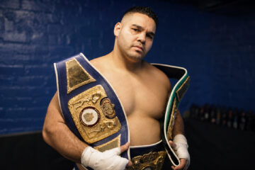 Erick Correa poses with championship belts in a blue-brick locker room.
