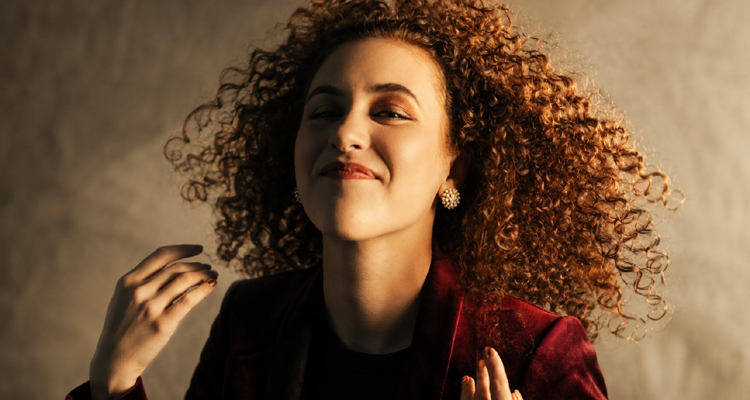 Gabrielle Lovelace wearing a deep red jacket with her curly hair in motion.