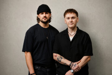 HOMECOMING members pose for a portrait against a light wall.