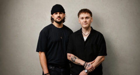 HOMECOMING members pose for a portrait against a light wall.