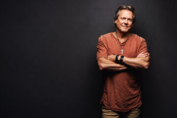 Howard Gripp standing with his arms crossed against a dark studio background.