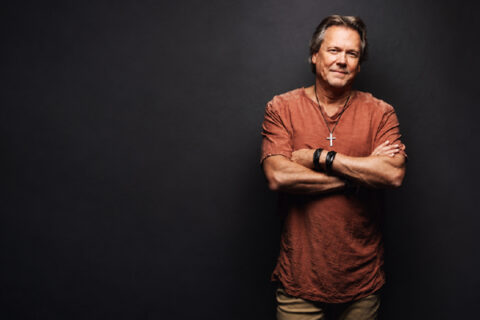 Howard Gripp standing with his arms crossed against a dark studio background.