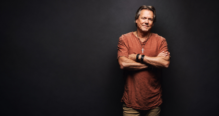 Howard Gripp standing with his arms crossed against a dark studio background.
