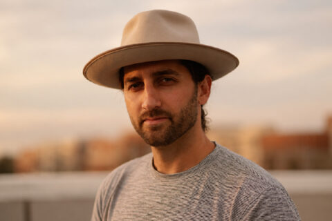 Justin Gambino wearing a tan wide-brim hat outdoors at golden hour.
