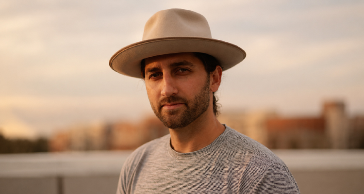 Justin Gambino wearing a tan wide-brim hat outdoors at golden hour.