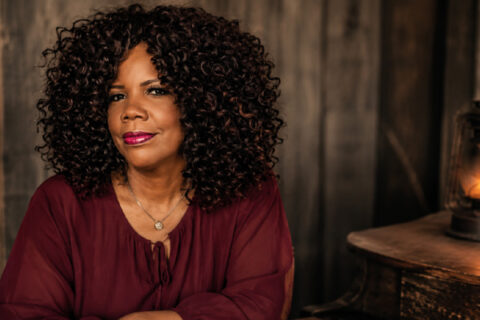 Lynda Randle seated beside a glowing lantern in a rustic setting.
