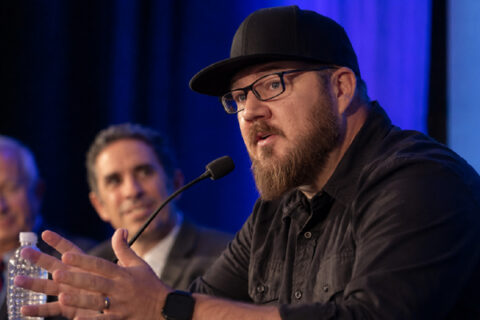 Panelist speaking at under blue stage lighting.