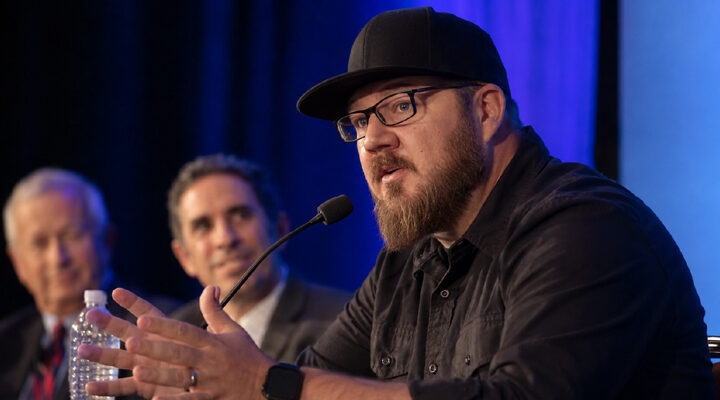 Panelist speaking at under blue stage lighting.