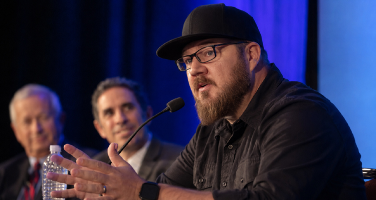 Panelist speaking at under blue stage lighting.