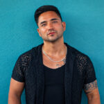 Sean Rodriguez standing against a teal wall in a black shirt.