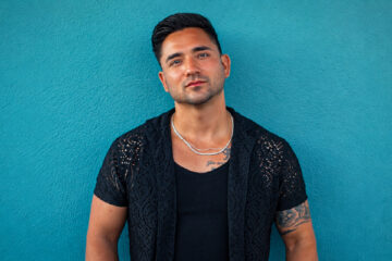 Sean Rodriguez standing against a teal wall in a black shirt.