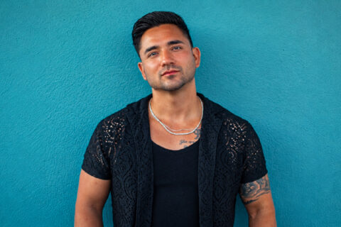 Sean Rodriguez standing against a teal wall in a black shirt.