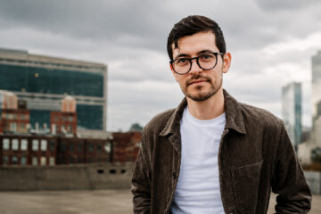 David Radford of The Gray Havens standing on a rooftop with a city skyline behind him.