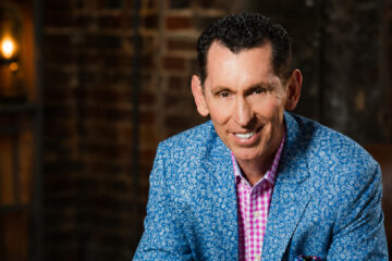 Tim Lovelace wearing a blue patterned blazer and smiling in a warmly lit room.