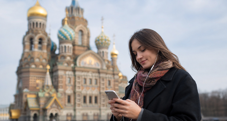 Woman listening to music on her phone in St. Petersburg with the Church of the Savior on Spilled Blood in the background.